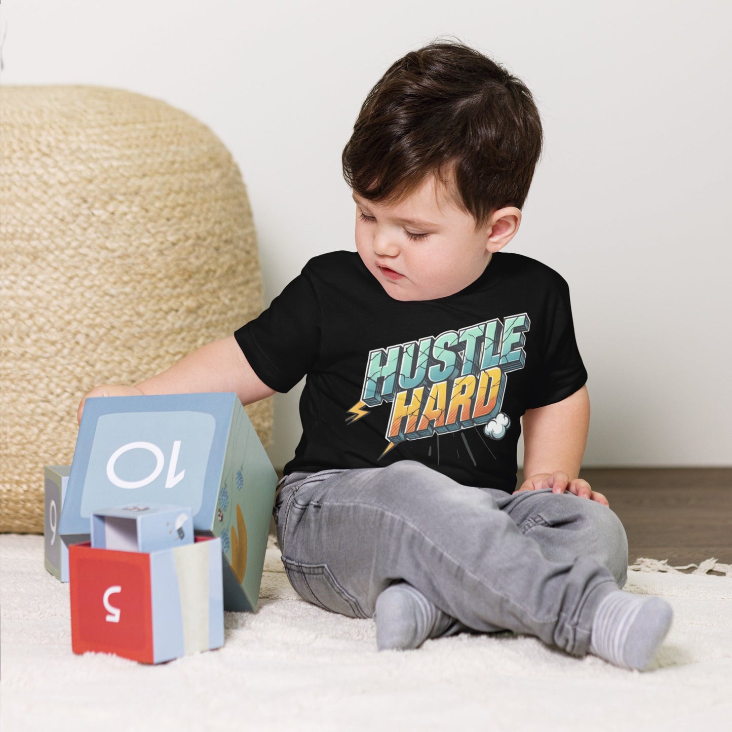 Toddler wearing black short sleeve tee with "Hustle Hard" print, playing with blocks.